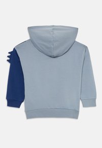 Felpa con cappuccio di colore grigio chiaro, una manica blu navy e tre piccoli picchi di tessuto sulla spalla sinistra.