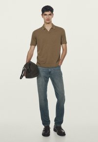 Brązowa koszulka polo z krótkim rękawem, jasnoniebieskie dżinsy, brązowe skórzane buty, trzymając ciemnobrązową torbę. Prosty, casualowy design z czystym wyglądem.