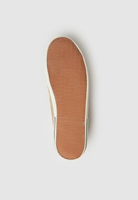 Suela de zapatilla de goma con un patrón texturizado en zigzag de color marrón-naranja. El costado presenta un borde blanco y una parte superior de fibra natural.