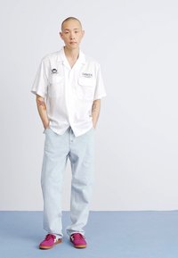 Camisa blanca de manga corta con dos bolsillos en el pecho, jeans holgados azules claros y zapatillas rosas. Tejido ligeramente texturizado y diseño casual.