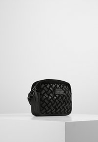 Musta kudottu laukku, jolla on jämäkkä muoto, sujuva nahkapinta, vetoketjukiinnitys ja irrotettava olkahihna.