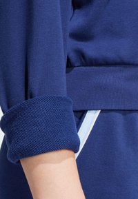 Marinblå sweatshirt-tyg har en strukturerad manschett med stickad yta. En ljusblå accentering syns vid sidosömmen och ger kontrast.