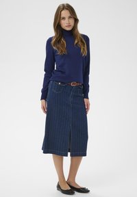 Pull à col roulé bleu marine associé à une jupe en denim avec rayures verticales, fente devant et ceinture marron. Des ballerines noires complètent la tenue.