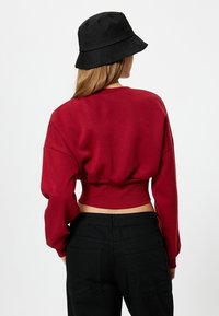 Rode, cropped sweatshirt gemaakt van zacht materiaal met lange, losse mouwen. Gecombineerd met een zwarte bucket hat en zwarte high-waisted broek.