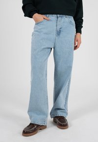 Lyseblå vide jeans med høy midje, to frontlommer og løs passform. Kombinert med mørkebrune sko og en mørkegrønn genser.