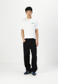 White short-sleeve t-shirt with colorful "Vacation" graphic, paired with black baggy pants and blue sneakers with three white stripes.