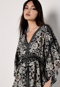 Schwarzes Kimono-Kleid mit floralen Motiven und weiten Ärmeln, das mit filigranen weißen Blumenmustern und einem V-Ausschnitt versehen ist. Es wird tailliert gebunden.