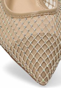 Zapato de tacón alto beige con punta afilada, que presenta un diseño de malla adornado con rhinestones iridiscentes sobre un fondo texturizado.