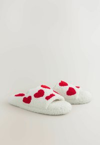 Chaussons en polaire blanche avec des motifs de cœurs rouges, design ouvert au niveau des orteils et texture douce. Convient pour une utilisation à l'intérieur.