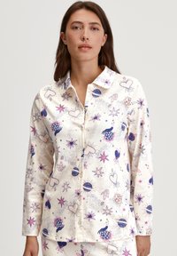 Knopenloze pyjama-top in crèmekleurige stof, met een speels patroon van harten, sterren en planeten in paarse en blauwe tinten.