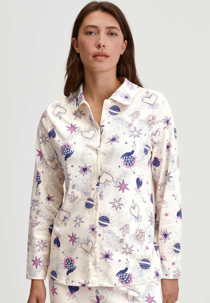 Knopenloze pyjama-top in crèmekleurige stof, met een speels patroon van harten, sterren en planeten in paarse en blauwe tinten.
