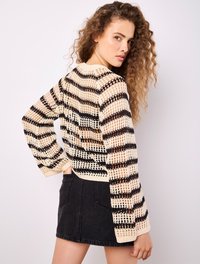 Gestreifter Strickpullover in Beige und Schwarz mit offener Maschenstruktur, mit langen Ärmeln und lockerem Schnitt, kombiniert mit einem schwarzen Jeansrock.