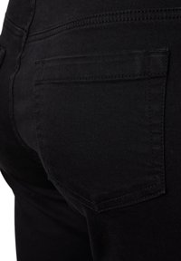 Vaqueros de mezclilla negra con un diseño ajustado, que cuentan con un bolsillo trasero único y costuras visibles en la cintura y en las costuras.