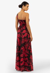 Robe maxi à épaule unique noire avec un motif floral rouge, dotée d'un corsage smocké et d'une jupe fluide. Tissu lisse avec des couleurs vibrantes.