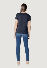 Maglietta navy a maniche corte con scollo rotondo, abbinata a jeans blu aderenti e scarpe con tacco trasparenti, vista da dietro.