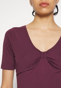 Haut bordeaux à manches courtes avec un décolleté en V profond et un détail froncé au centre. Tissu doux avec une texture lisse.