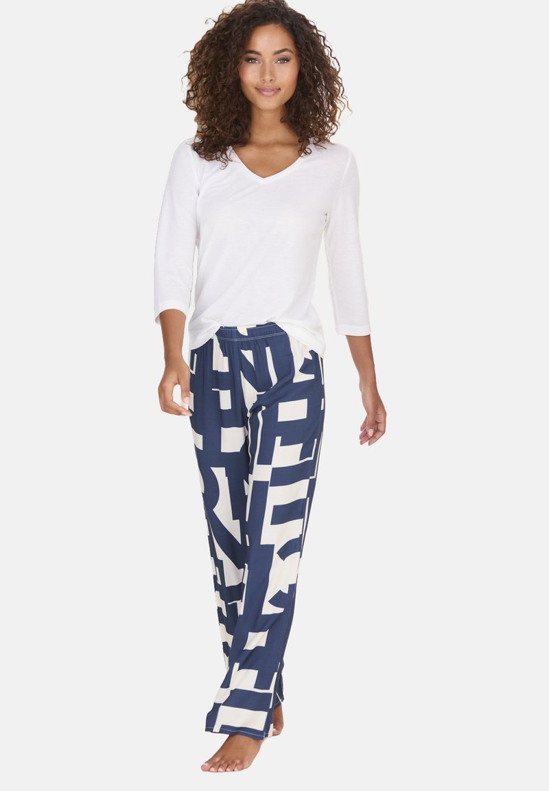 White v-neck long-sleeve top paired with navy wide-leg pants featuring bold cream geometric patterns. Soft, lightweight fabric.