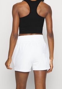 Musta ribatta crop top, jossa on kilpailijatyyppinen selkäosa, yhdistettynä valkoisiin elastisiin shortsikuteisiin. Kankaan pinta näyttää sileältä ja siinä on kevyt rakenne.