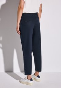 Granatowe, lekkie spodnie o luźnym kroju, z elastycznym pasem i dwoma tylnymi kieszeniami. Połączone z białymi trampkami.