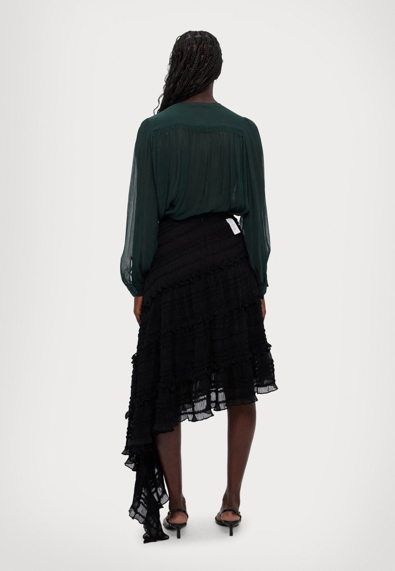 Zwarte gerimpelde rok met asymmetrische zoom, gecombineerd met een donkergroene transparante blouse met lange mouwen. Gladde textuur en vloeiend ontwerp.