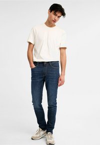 Vit t-shirt med kort ärm kombinerad med blå denimjeans, med en klassisk passform, subtil textur och beige sneakers för kontrast.