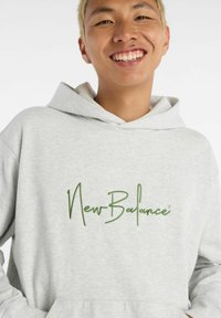 Grey hoodie made of soft fabric with a kangaroo pocket, featuring green embroidered "NewBalance" logo on the front.