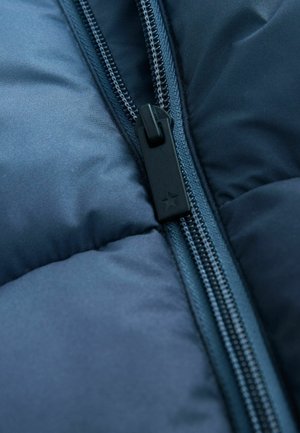 Zbliżenie czarnego plastikowego suwaczka z symbolem gwiazdy na granatowej, pikowanej tkaninie kurtki.