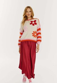 Wielokolorowy sweter z różowymi i czerwonymi kwiatami na kremowym tle, zestawiony z długą burgundową spódnicą i różowymi trampkami.