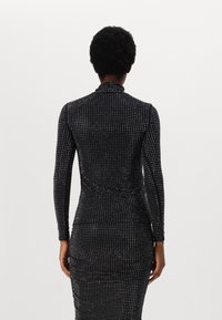 Black long-sleeve dress featuring a fitted silhouette with a textured pattern of small white dots throughout. High collar design.