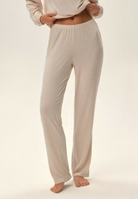 Jasnobeżowe, prążkowane spodnie dresowe z elastycznym pasem, prostymi nogawkami i miękką fakturą, zaprojektowane z myślą o komforcie i swobodzie ruchów.