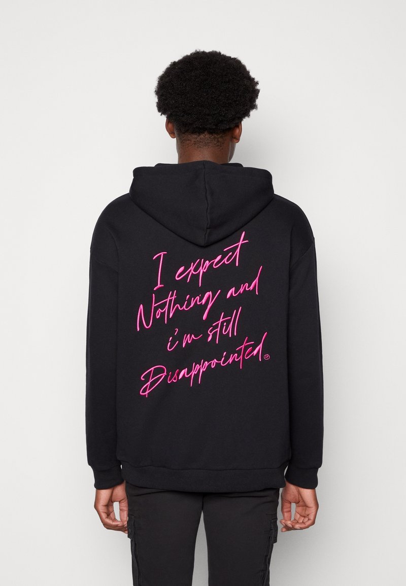 Svart hoodie med stor, rosa handskriven text på baksidan. Materialet verkar mjukt med en mysig textur och huva med dragsko.
