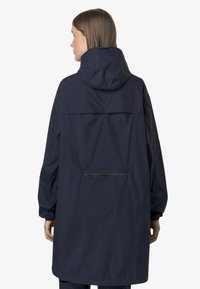 Veste imperméable bleu marine avec capuche, manches longues et détail de ventilation au dos. Comprend une poche zippée avec une fermeture éclair jaune contrastante.