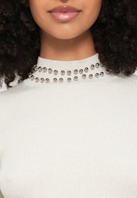 Ανοιχτό γκρι ριπ τοπ με ψηλό λαιμόκοψη στολισμένη με ασημένια στρογγυλά τρουκς γύρω από το γιακά. Απαλή υφή με εφαρμοστή σχεδίαση.