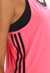 Różowy sportowy top na ramiączkach z czarnymi paskami po bokach i okrągłym dekoltem, wykonany z oddychającej tkaniny o gładkiej fakturze.