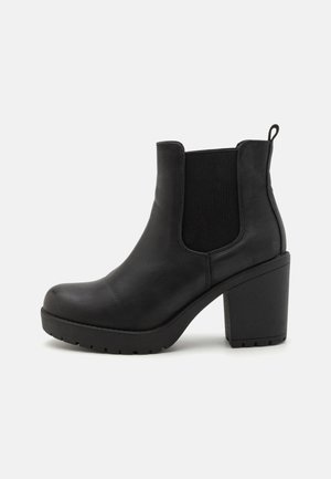 Bottes noires à la cheville en cuir synthétique lisse avec un talon carré épais et des panneaux latéraux élastiques. Semelle extérieure texturée pour une meilleure adhérence.