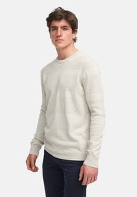 Hellgrauer Strickpullover mit strukturierten horizontalen Streifen, rundem Halsausschnitt und langen Ärmeln, kombiniert mit dunklen Hosen.