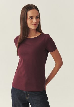 Bordowa bluzka z krótkim rękawem, okrągłym dekoltem, gładką fakturą, dopasowanym krojem i subtelną elastycznością; w zestawieniu z ciemnymi jeansami denim.