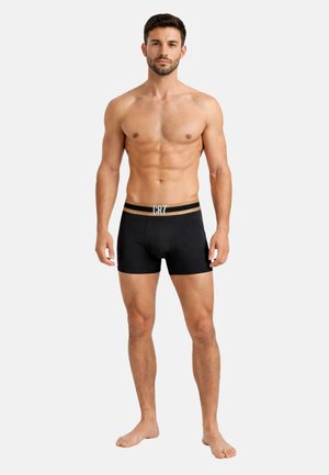 Atletisk mand stående barfodet iført sorte boxershorts med CR7-logo på linningen mod en ensartet lys baggrund.