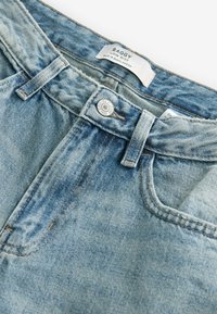Baggy low-rise jeans in lichtblauwe denim met vervaagde plekken, voorzien van een metalen knoopsluiting en zichtbare stiksels langs de naden.