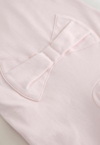 Lyserød bomuldsstof med en stor, bueformet detalje. Buen har folded kanter og en glat tekstur, der komplementerer skjortens design.