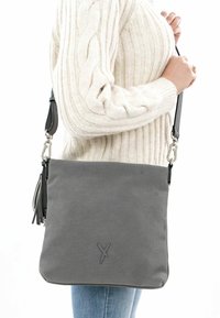 Gray perforated handbag with a flat design, featuring a detachable shoulder strap, silver hardware, and a decorative tassel accent.