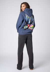 Blauwe hoodie met een bloemenprint op de achterkant, met levendige kleuren. Gecombineerd met donkergrijze broek en een ontspannen pasvorm.