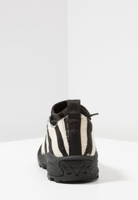 Botín hasta el tobillo con estampado de cebra, suela de goma negra y parte superior texturizada. Cuenta con una lengüeta de tela en el talón y un lateral elástico para facilitar su uso.