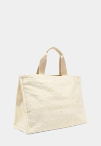 Crèmekleurige canvas draagtas met geperst merklogo, gestructureerde vorm, bovenhandvatten en een textuurrijke afwerking. Afmetingen geschikt voor dagelijks gebruik.