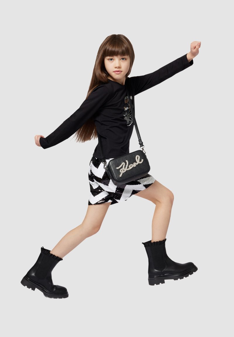 Zwarte longsleeve top, glinsterende zwart-witte zigzag rok, kleine zwarte tas met "Karl" in het wit en zwarte enkellaarsjes met gerimpelde toppen.