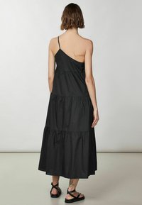 Vestido maxi negro de capas con una tira de hombro asimétrica, hecho de tejido ligero, que presenta una textura recogida y una silueta fluida.