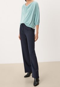 Top verde menta, drappeggiato, con maniche corte abbinato a pantaloni larghi blu navy e stivaletti neri con tacco, caratterizzato da una texture liscia e un design casual.