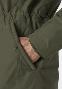 Chaqueta verde olivo con un bolsillo lateral, puños elásticos y cintura ajustada para un aspecto entallado. Textura de tela suave y a prueba de agua.
