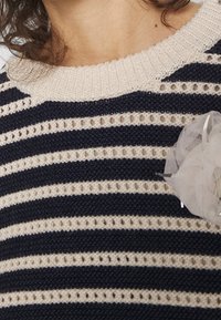 Pull en maille rayé bleu marine et crème avec un motif texturé et un tissage ouvert, présentant un accent décoratif en tulle sur le côté droit.