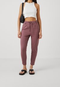 Lätta, figursydda mauve byxor med elastisk midja, snörning och anklar. Kombineras med en vit kortärmad tanktop och svarta sandaler.
